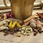 Image showing dry spices used to make ras el hanout at the base of a brass mortar and pestle.