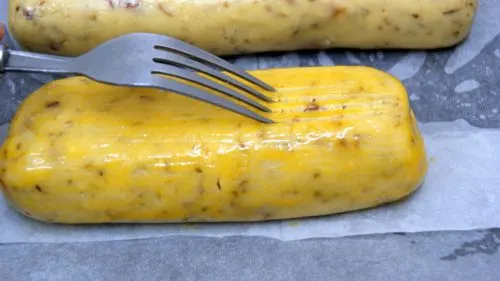 Applying parallel patterns on the egg wash on top of a large stick of dough