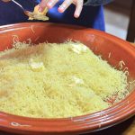 Several pats of butter can be seen on top of a large shallow dish of steamed broken angel hair pasta.