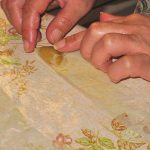 Close-up photo of hands folding almond paste into a triangular pastry with a narrow strip of warqa pastry.
