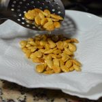 Fried almonds are being transferred from a slotted ladle to a plate lined with paper towels.