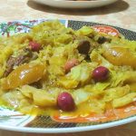 Moroccan stewed cabbage is served on a decorated plate. Pieces of meat can be seen in the cabbage, and the dish is decorated with wedges of preserved lemon and olives.