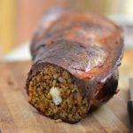 Close-up view of veal spleen stuffed with a Moroccan mixture of kefta and rice sits on a wooden cutting board. The spleen has been sliced to reveal the filling. A knife sits on the cutting board next to the stuffed spleen.